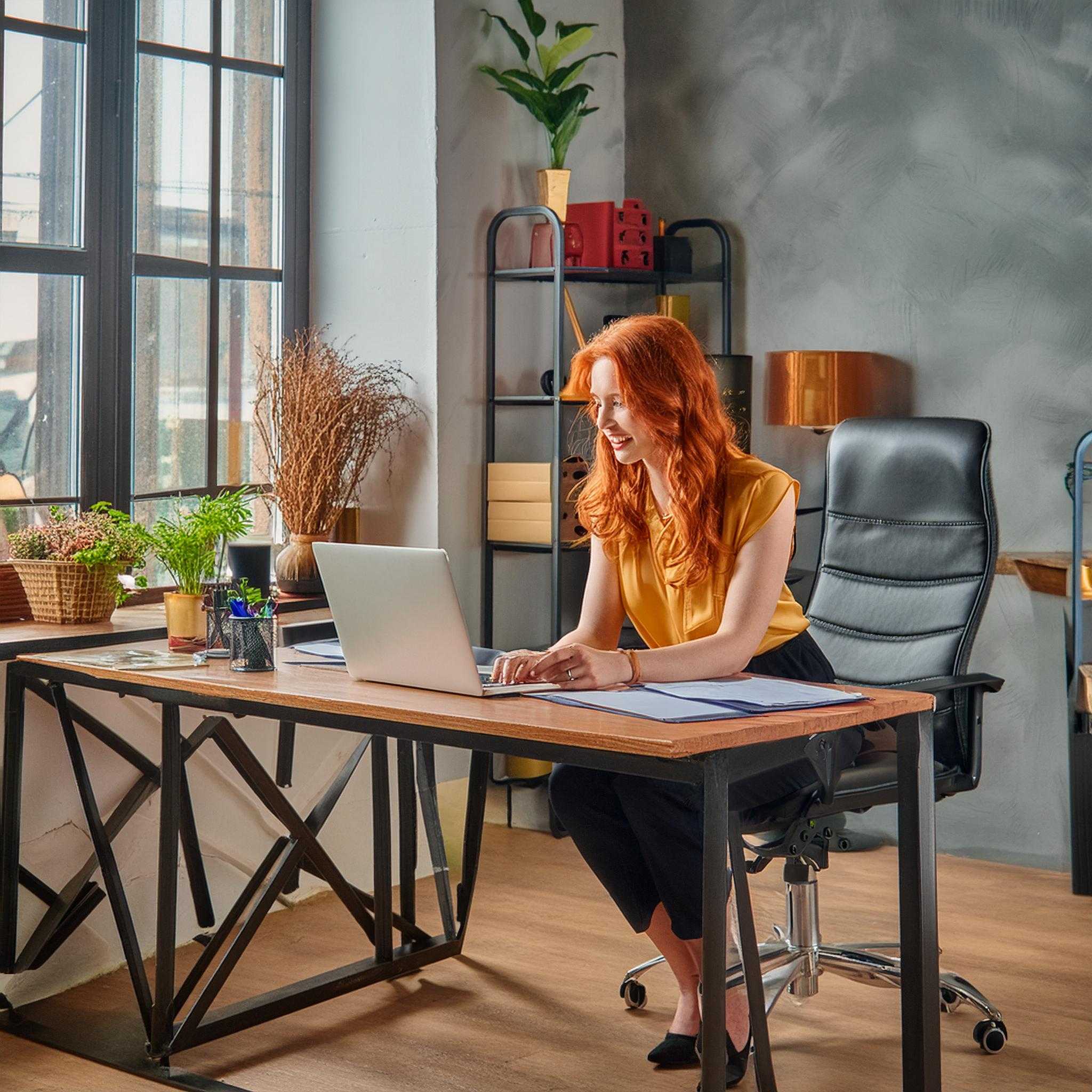 A woman working on a laptop at a desk in a modern office with plants and decorations.